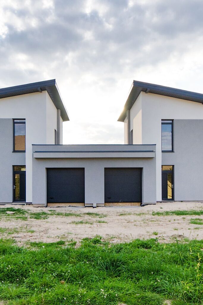 Front view of twin modern houses with a symmetrical architectural design under a cloudy sky.